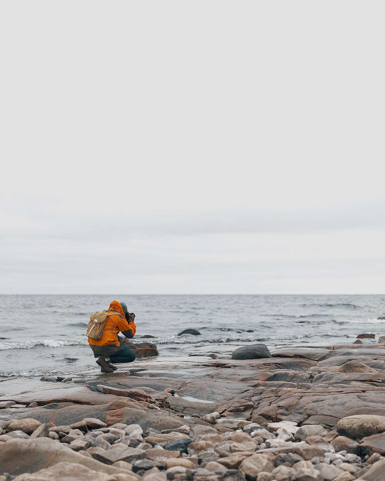 A person crouching on a rocky shore to photograph the landscape